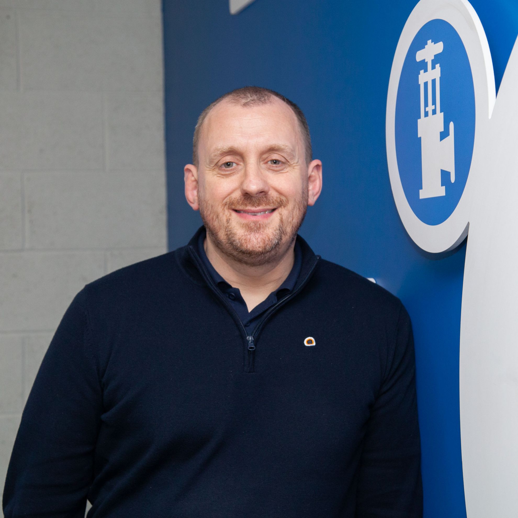 Man stood smiling with his arms folded in front of an open control panel on an industrial boiler 